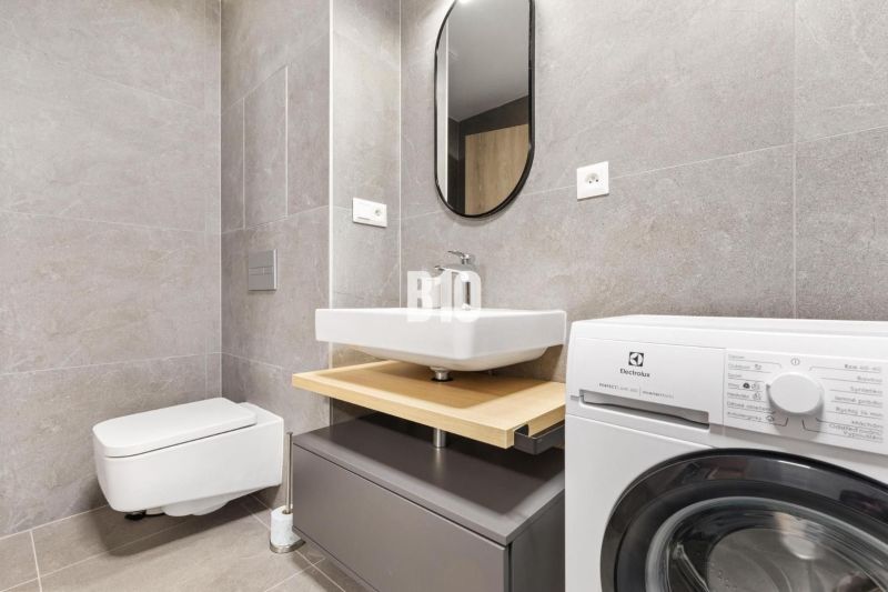Badezimmer in einer Einzimmerwohnung mit moderner Waschmaschine und grauen Fliesen.