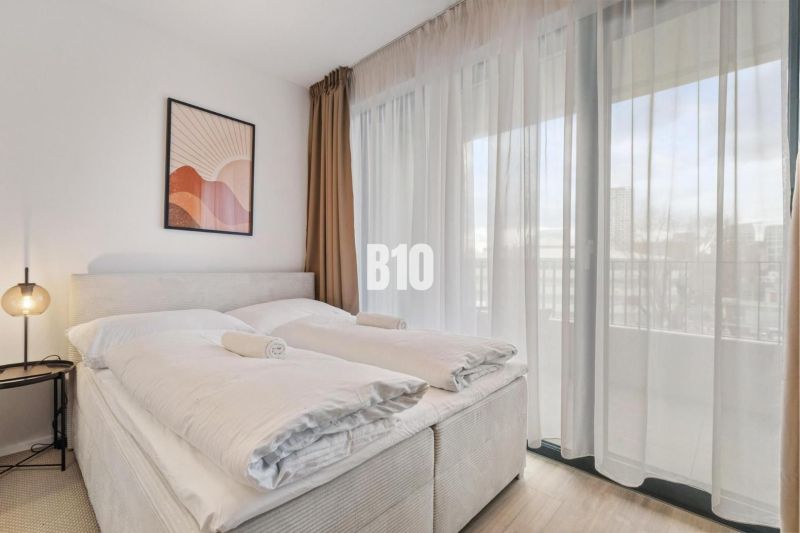 Schlafzimmer mit Bett, Nachttisch, Bild und durchsichtigen Vorhängen in einer Einzimmerwohnung.