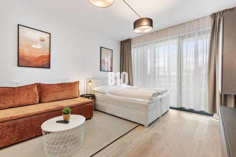 Wohnbereich einer Einzimmerwohnung mit Sofa, Bett und Boden in Holzoptik.