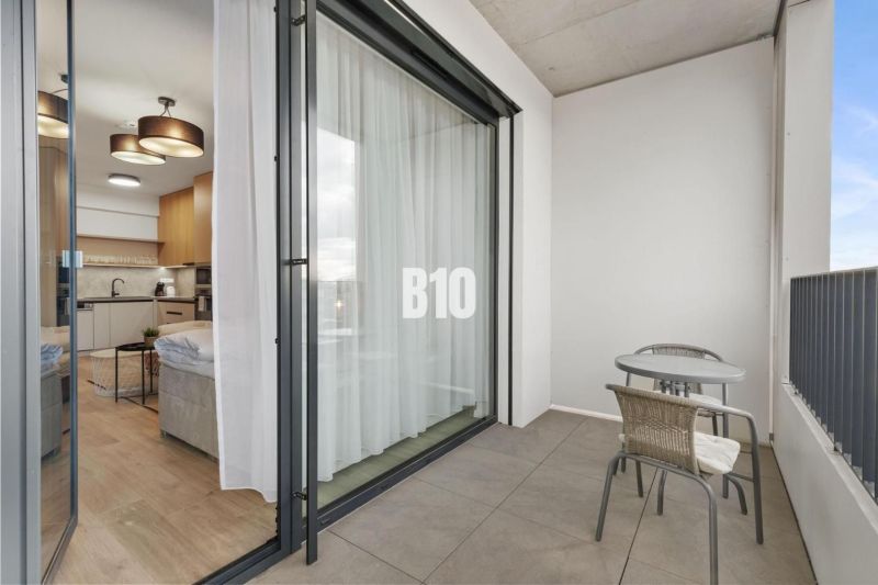 Ein Balkon mit Sitzgelegenheit und Blick in eine Einzimmerwohnung durch Schiebetüren.