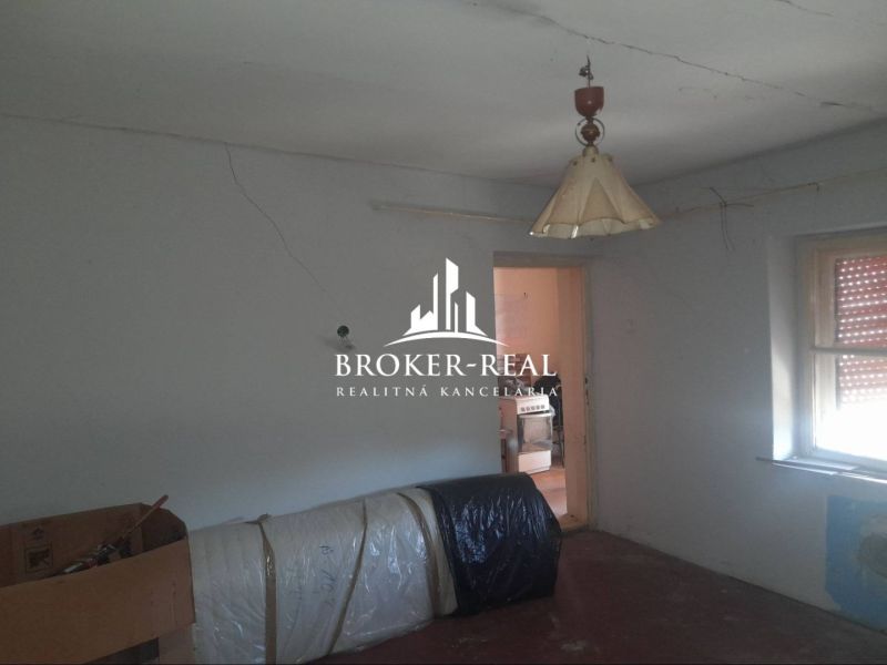 Das Innere eines Einfamilienhauses mit einfacher Einrichtung, einem älteren Kronleuchter und einem Fenster mit Jalousie.