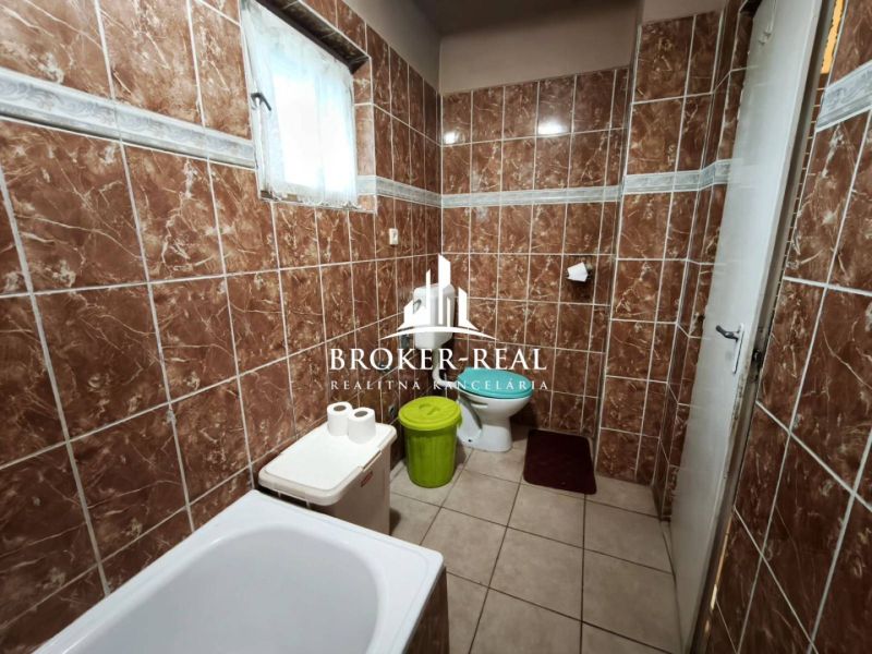 Ein Badezimmer mit braunen Fliesen, einer Badewanne, einer Toilette und einem Mülleimer in einem Einfamilienhaus.