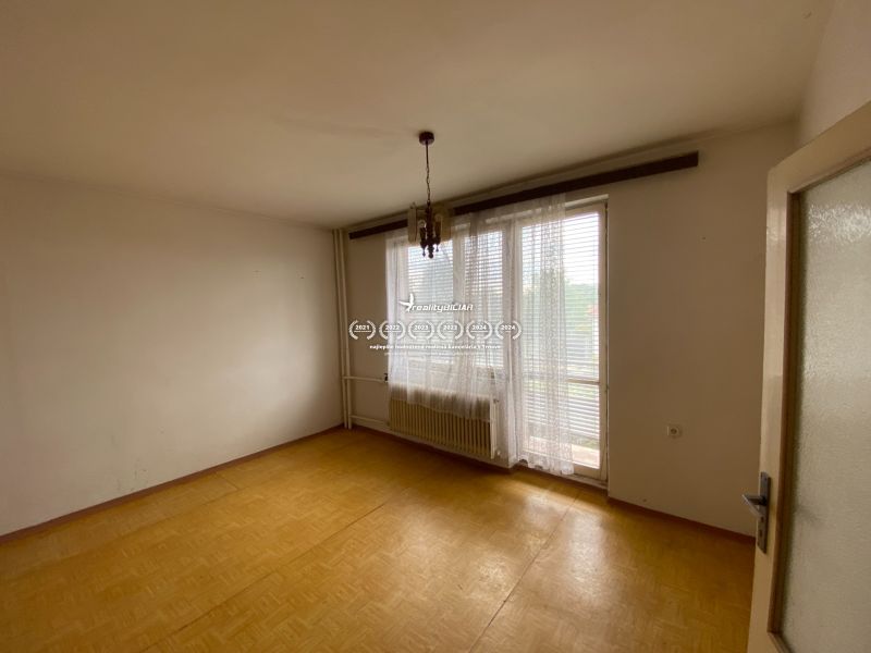 Ein leerer Raum in einem Einfamilienhaus mit einem Fenster, Vorhängen und einem Boden in Holzoptik.
