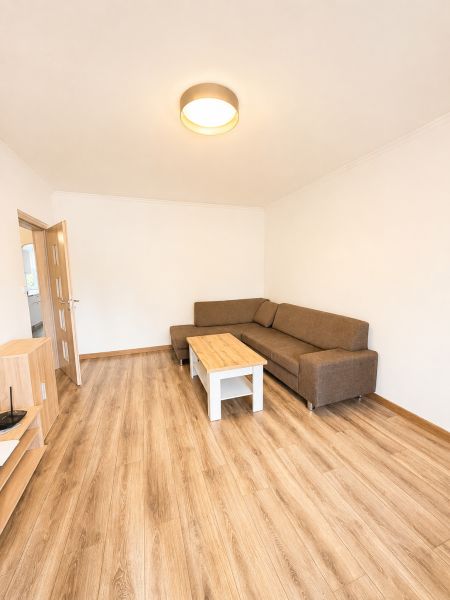 Wohnzimmer mit braunem Sofa und Tisch auf einem Boden mit Holzdekor in einer 3-Zimmer-Wohnung.