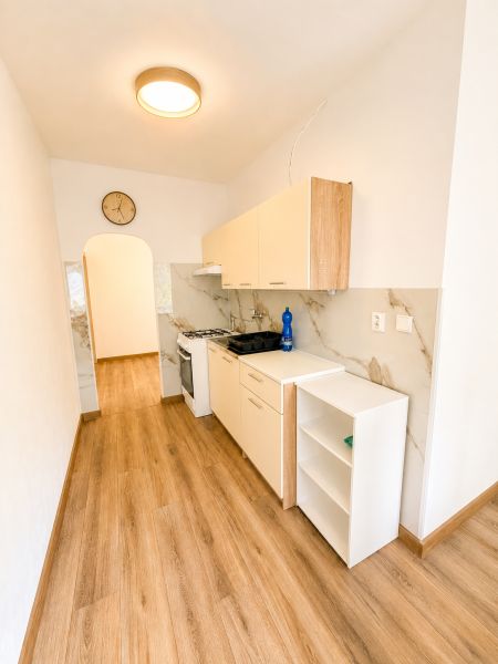 Eine schmale Küche in einer 3-Zimmer-Wohnung mit einem Holzboden und hellen Schränken.