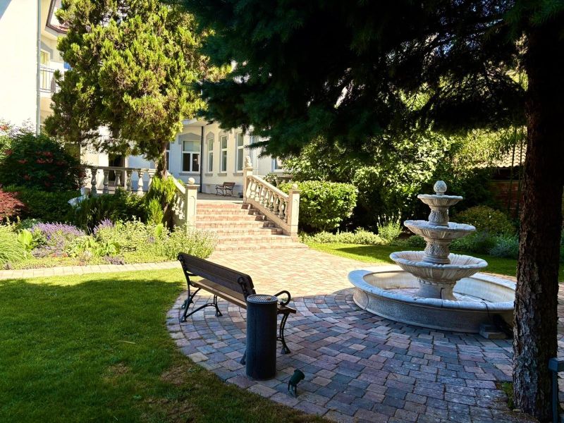 Ein Garten mit einem Brunnen, einer Bank und Grünflächen vor dem Gebäude.