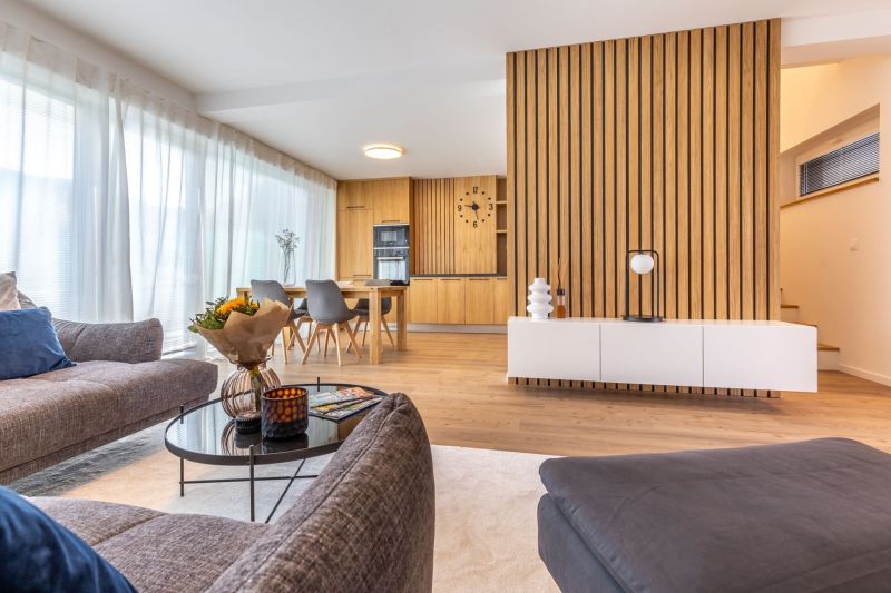 Wohnzimmer in einem Einfamilienhaus mit Holzboden und Essbereich im Hintergrund.