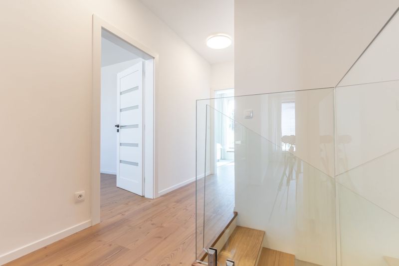 Innenraum eines Einfamilienhauses mit Holzboden und Glasgeländer an der Treppe.