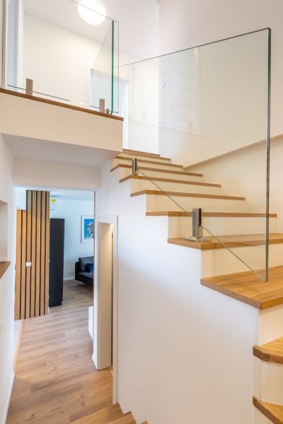 Innenraum eines Einfamilienhauses mit Holztreppe, Glasgeländer und Boden mit Holzdekor.