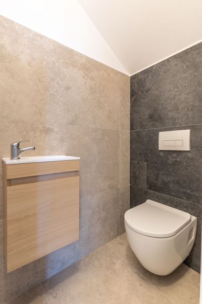 Badezimmer in einem Einfamilienhaus mit Toilette und Holzschrank unter dem Waschbecken.