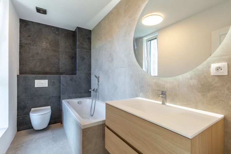 Badezimmer in einem Einfamilienhaus mit Badewanne, Waschbecken und Fliesen in dunklen Tönen.