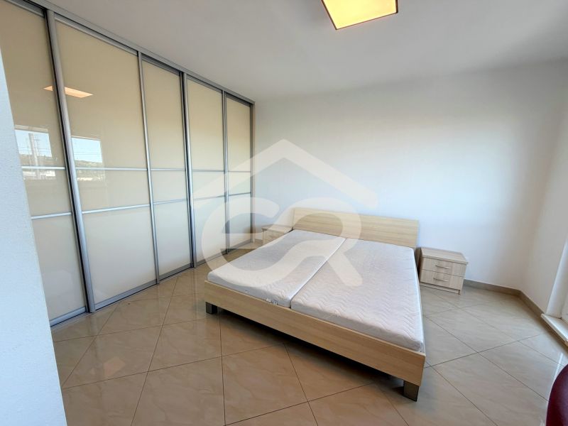 Helles Schlafzimmer mit Schiebetürenschrank, Bett und Fliesenboden in einer Einzimmerwohnung.
