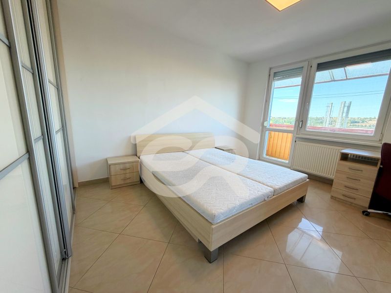 Helles Schlafzimmer in einer Einzimmerwohnung mit Bett, Schrank und Balkon.