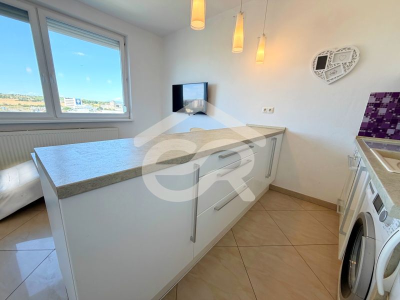 Küche in einer Einzimmerwohnung mit Waschmaschine, weißen Schränken und Arbeitsplatte.