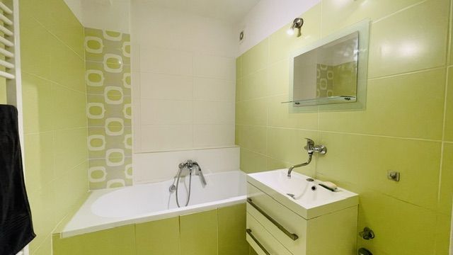 Grün-weißes Badezimmer mit Badewanne und Waschbecken in einer 3-Zimmer-Wohnung.