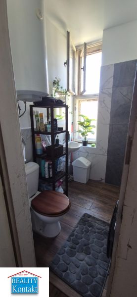Badezimmer in einer 2-Zimmer-Wohnung mit Fenster, Regalen und Boden in Holzoptik.
