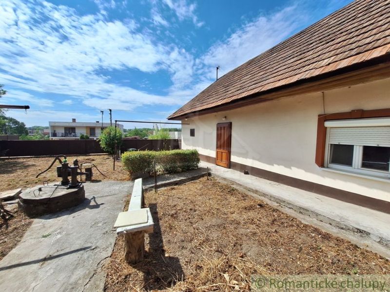 Ein Einfamilienhaus in Kamenica nad Hronom mit Hof, Brunnen und Bank auf einem sonnigen Grundstück.