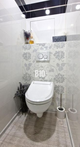 Ein einfach eingerichtetes WC mit dekorativen Fliesen und einem Boden in Holzoptik.