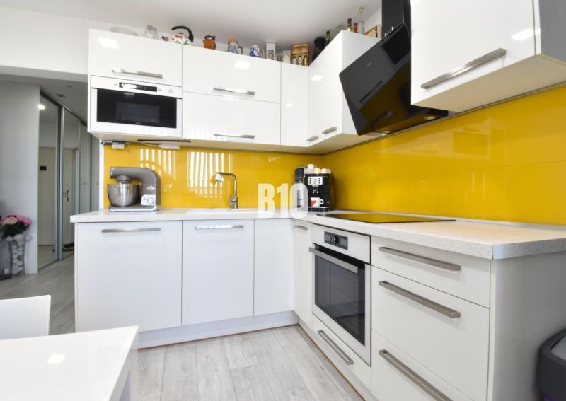Küche in einer 3-Zimmer-Wohnung mit weißer Küchenzeile und gelben Fliesen.
