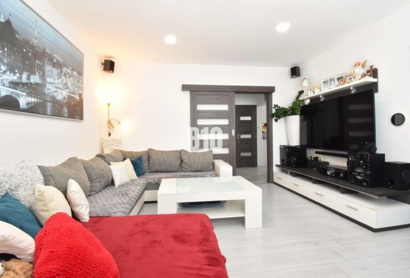 Wohnzimmer in einer 3-Zimmer-Wohnung mit Ecksofa, Fernseher und Boden in Holzoptik.