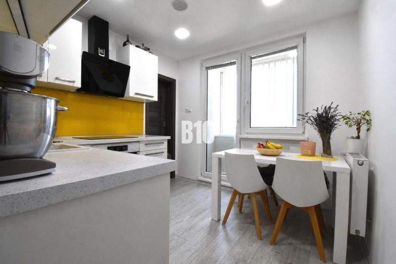 Küche in einer 3-Zimmer-Wohnung mit weißen Möbeln und gelben Fliesen bei dem Herd.