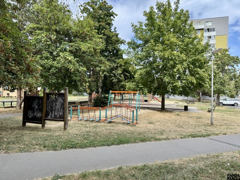 Ein Kinderspielplatz, umgeben von Bäumen, im Park der Stadt Topoľčany, in der Nähe einer Einzimmerwohnung.