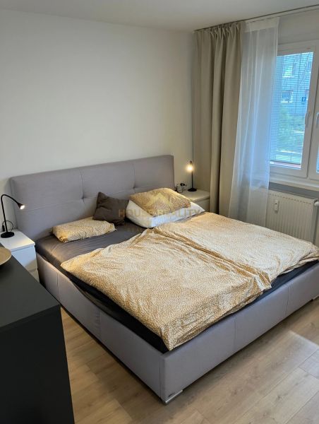 Schlafzimmer mit großem Bett, Nachttischen und Boden mit Holzdekor in einer 3-Zimmer-Wohnung.