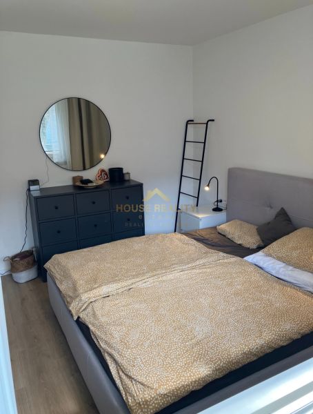 Schlafzimmer mit Bett, Kommode und rundem Spiegel in einer 3-Zimmer-Wohnung.