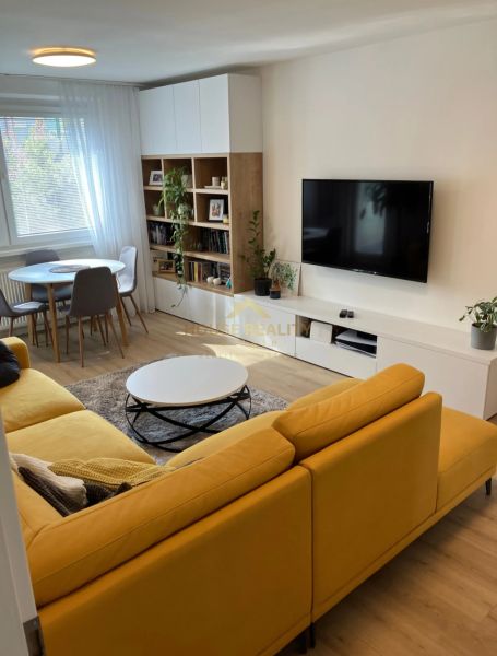 Wohnzimmer in einer 3-Zimmer-Wohnung mit einem bequemen Sofa, einem Esstisch und einem Boden in Holzoptik.