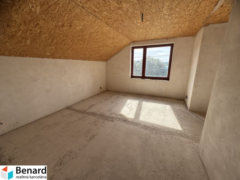 Innenraum eines Einfamilienhauses mit Fenster, schräger Decke und unbehandeltem Boden.