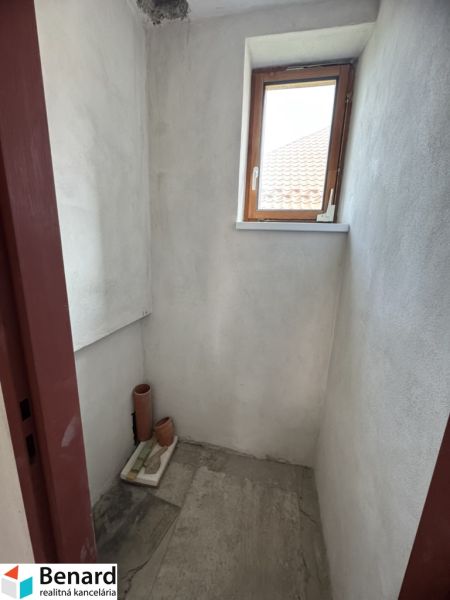 Ein kleiner Raum mit einem Fenster in einem Einfamilienhaus, unverputzte Wände, Fliesenboden.
