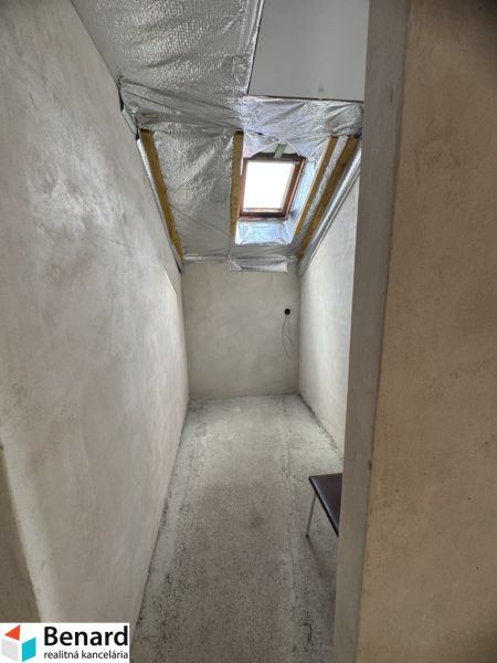 Ein schmaler Raum mit Betonboden und Dachfenster in einem Einfamilienhaus.