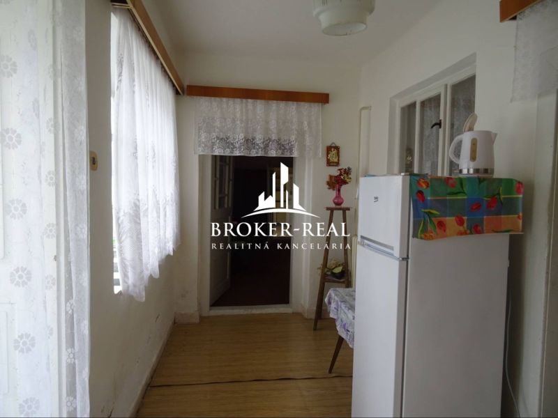 Innenraum eines Einfamilienhauses mit einem weißen Kühlschrank und einem dekorierten Boden in Holzoptik.