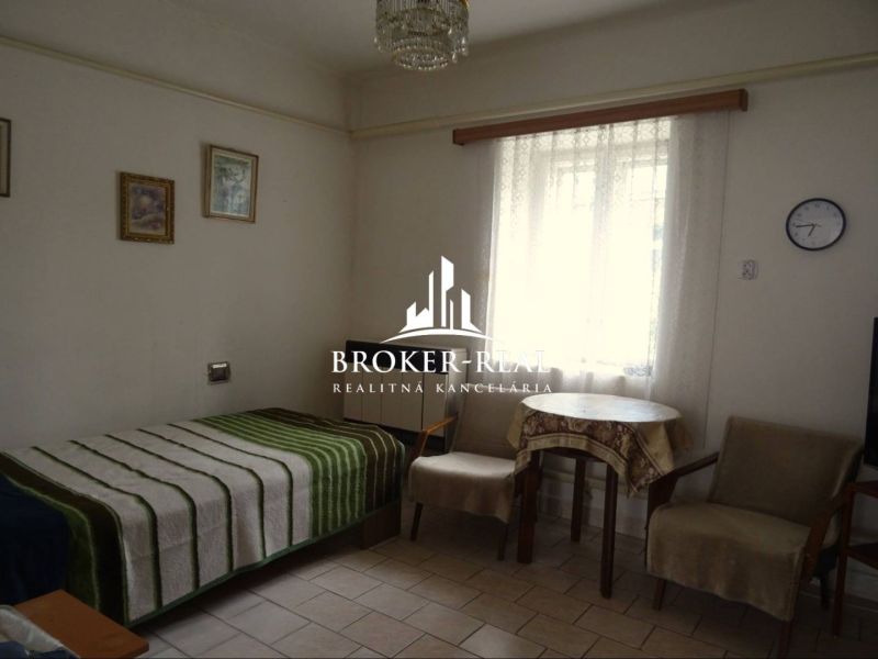 Ein Zimmer in einem Einfamilienhaus mit Bett, Sesseln und Tisch, dekorative Bilder an der Wand.