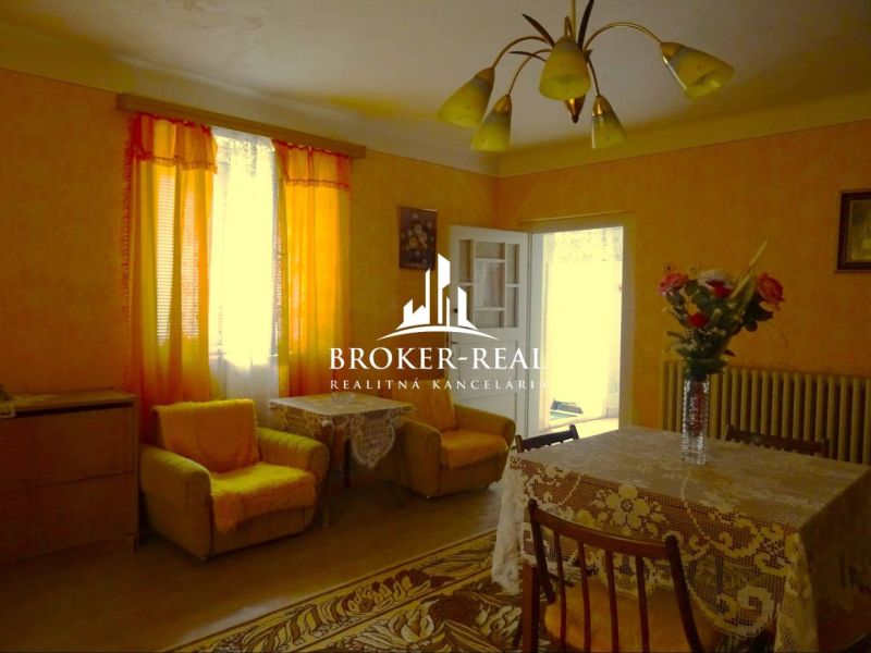 Ein Wohnzimmer in einem Einfamilienhaus mit orangefarbenen Vorhängen und einem Tisch mit einer Tischdecke.