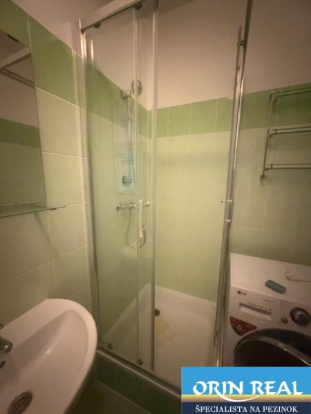 Badezimmer in einem Einzimmerapartment mit Duschkabine, Waschmaschine und Waschbecken mit Keramikfliesen.