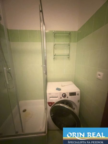 Badezimmer in einem Einzimmerapartment mit Duschkabine und Waschmaschine, grüne Fliesen.