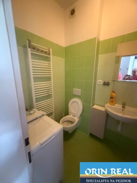 Badezimmer eines Einzimmerapartments mit grünen Fliesen, Waschbecken, Toilette und Waschmaschine.