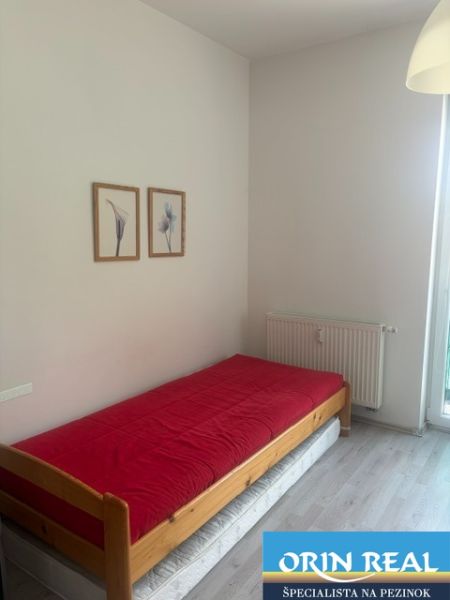 Einzimmerwohnung mit Bett, roter Decke und Boden in Holzoptik.