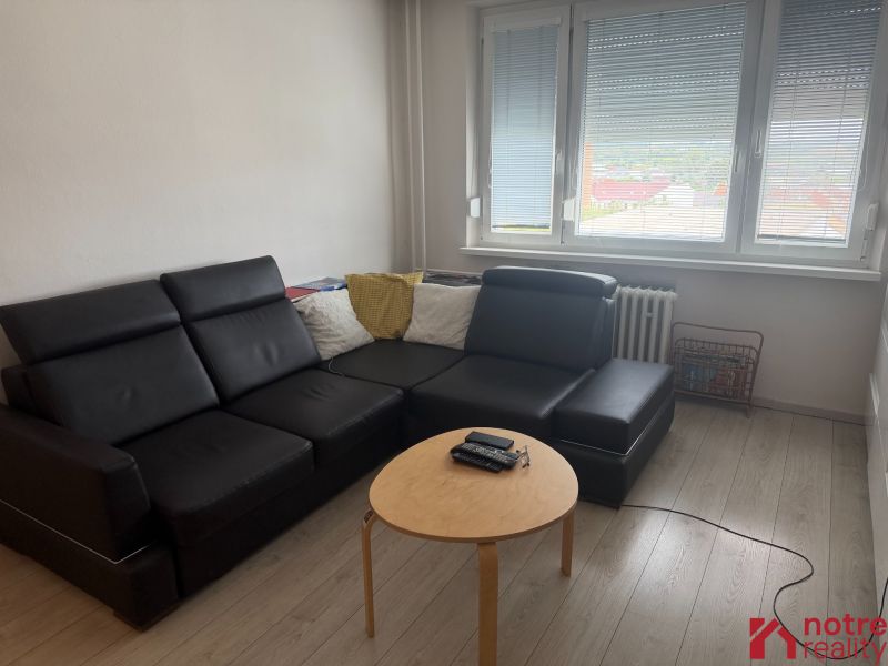 Wohnzimmer in einer 2-Zimmer-Wohnung mit schwarzem Sofa und Holzboden.