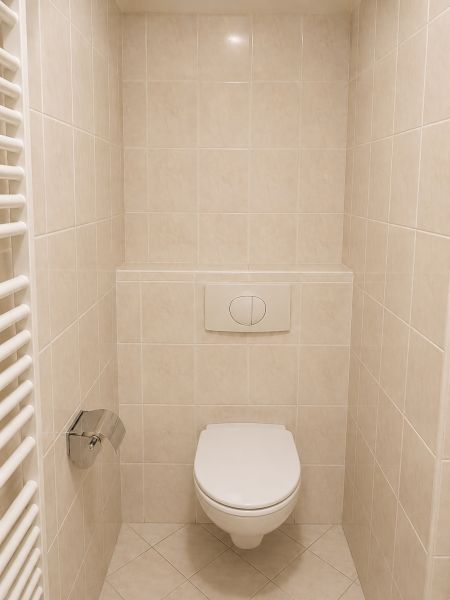 Badezimmer-WC in einer 2-Zimmer-Wohnung mit Fliesenboden und wandmontiertem Spülsystem.
