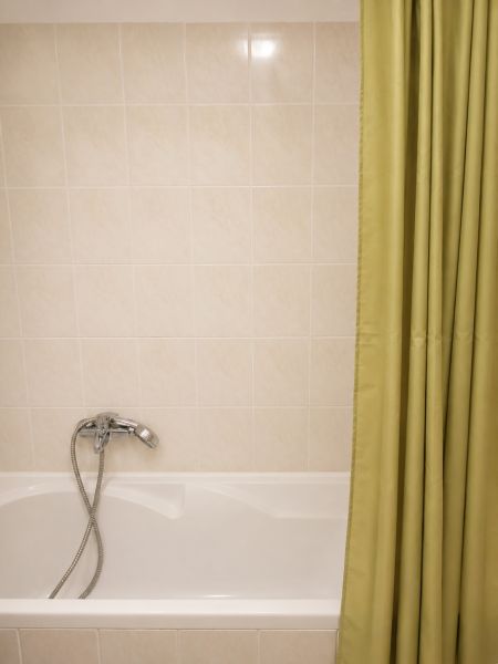 Badezimmer mit Badewanne, Duschvorhang und hellen Fliesen in einer 2-Zimmer-Wohnung.