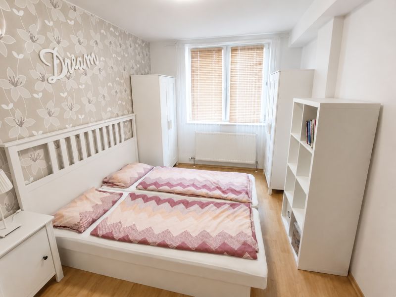 Helles Schlafzimmer mit Doppelbett, Blumen-Tapete und Holzboden.