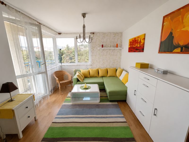 Wohnzimmer mit Ecksofa, Holzboden und buntem Teppich.