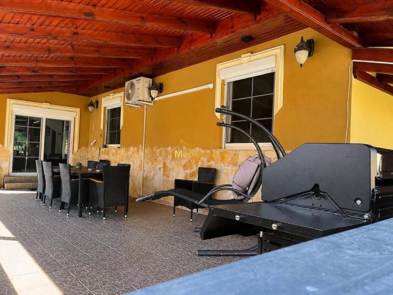 Die Terrasse des Einfamilienhauses in Darnózseli mit Rattanmöbeln und einem Grill unter einer Holzdecke.