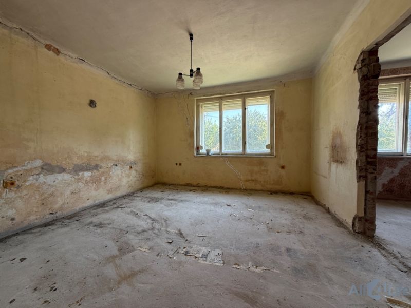 Ein Zimmer in einem Einfamilienhaus mit einem Fenster, abgebröckeltem Putz und unfertigem Boden.