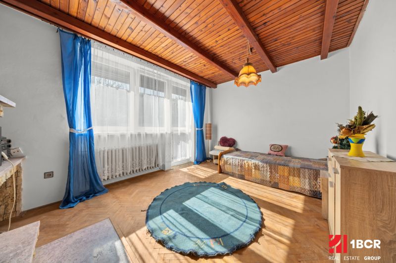Ein Zimmer in einem Einfamilienhaus mit einem Boden in Holzoptik, blauen Vorhängen und einem großen Fenster.