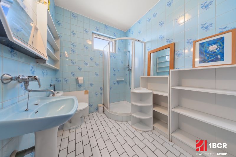Ein Badezimmer mit blauen Fliesen, einer Duschkabine und weißen Möbeln in einem Einfamilienhaus.