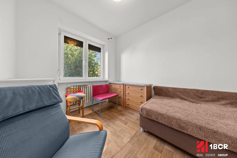 Ein Zimmer mit einem großen Fenster, einem Stuhl, einer Kommode und einem Boden mit Holzdekor in einem Einfamilienhaus.