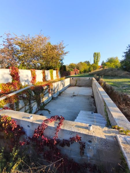 Ein unvollendetes Schwimmbecken, umgeben von Grün und Kletterpflanzen, bei einem Einfamilienhaus in Zlaté Moravce.
